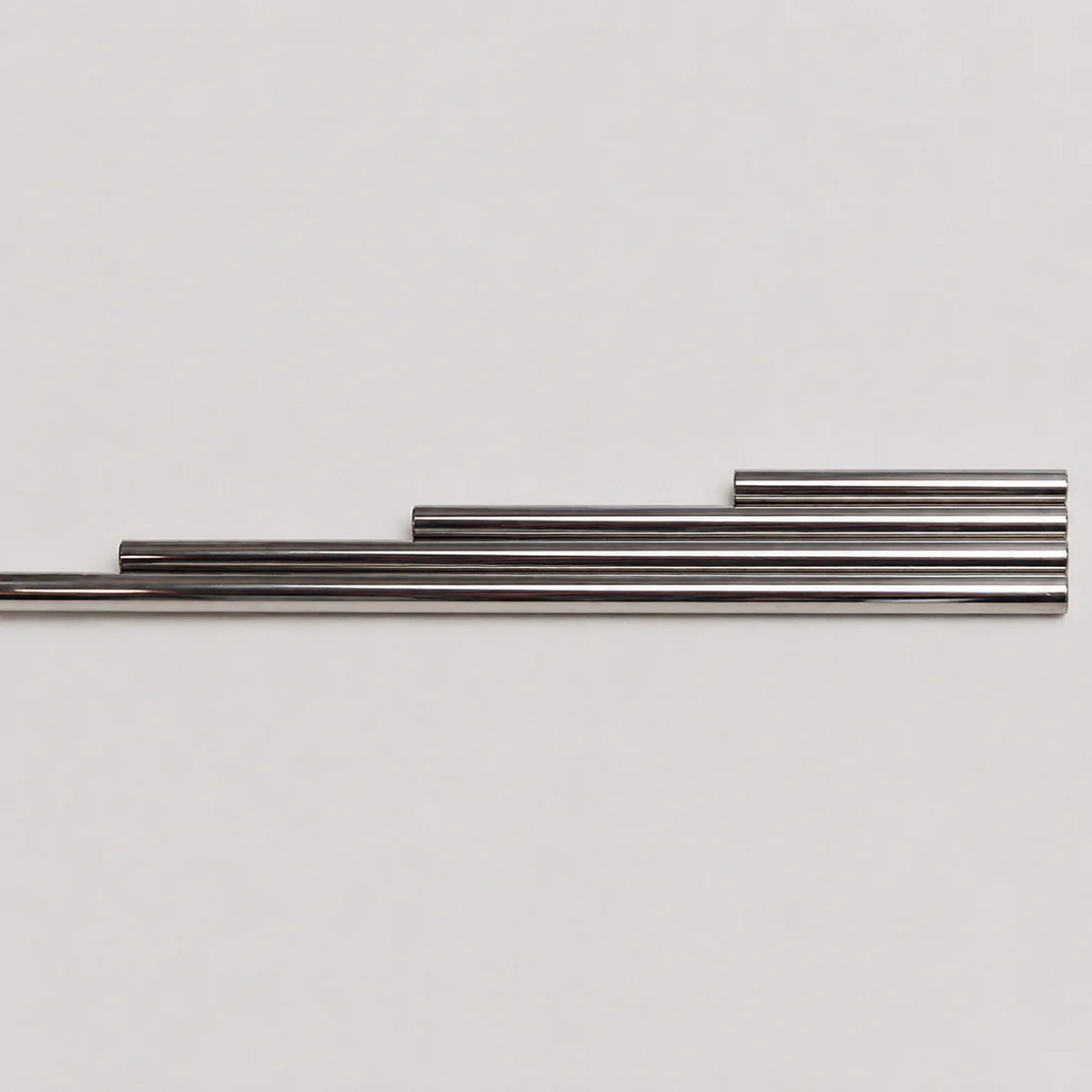 Four metallic silver rods of varying lengths arranged in a stepped horizontal layout against a plain light gray background.