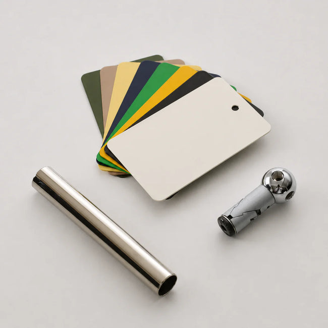 A set of metal color sample cards fanned out behind a silver cylindrical tube and a chrome ball valve fitting on a light gray background.