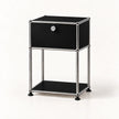 A modern black and chrome storage cabinet with a single drawer, a lock, and an open lower shelf, set against a plain white background.