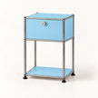 A light blue modular storage cabinet with a chrome metal frame, featuring a single drawer with a round silver knob and an open lower shelf, set against a plain white background.