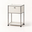 A modern two-tier nightstand featuring a silver chrome tubular metal frame, cream-colored panels, and a single lockable drawer on the top tier with a round silver knob.