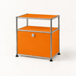 An orange modular storage cabinet with a chrome metal frame and black feet, featuring a lockable lower compartment and an open upper shelf.