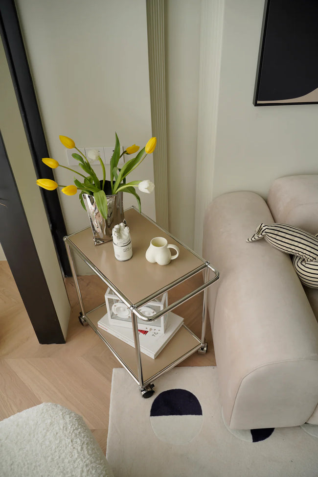 Replica USM modular small stroage sart with flowers and a cup next to a sofa in a living room.
