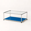 A modern two-tier coffee table with a clear glass top, a stainless metal frame, and a vibrant blue lower shelf, shown on a clean white background.