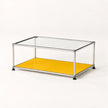 A modern rectangular coffee table with a clear glass top, a stainless metal frame, and a bright yellow metal lower shelf, shown on a clean white background.