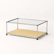 A modern two-tier coffee table with a clear glass top, a metallic stainless frame, and a light beige lower shelf, shown on a plain white background.