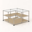 A modular two-tier storage organizer with a chrome metal frame, clear glass top panels, and beige metal shelves, shown on a light cream background.