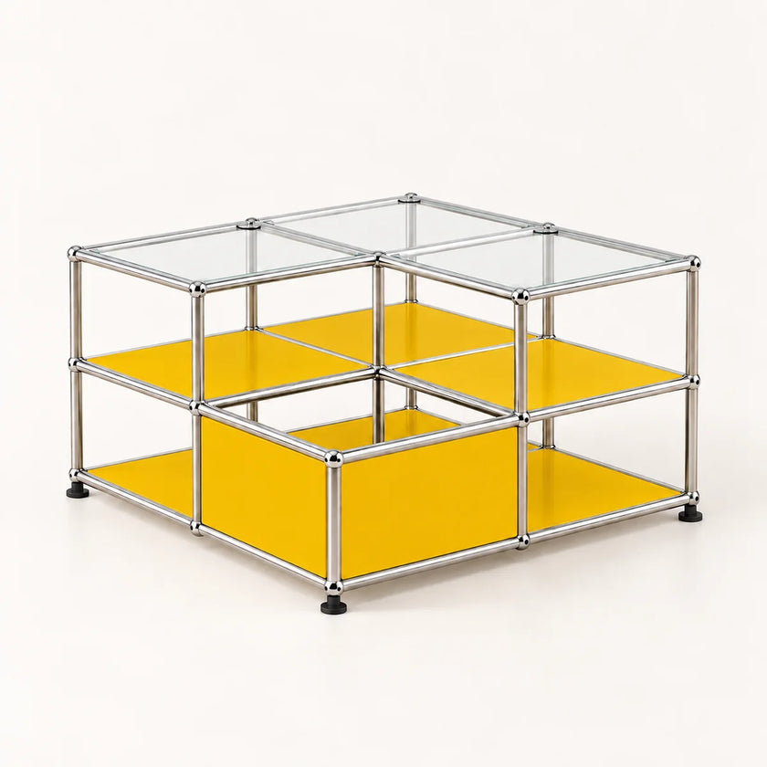 A modular storage organizer made of a chrome metal frame with clear glass panels on top and bright yellow shelves on the sides and bottom, shown on a light cream background.