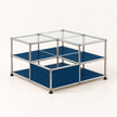 A modular two-tier storage unit with a chrome metal frame, clear glass top panels, and dark blue shelves, shown on a light beige background.