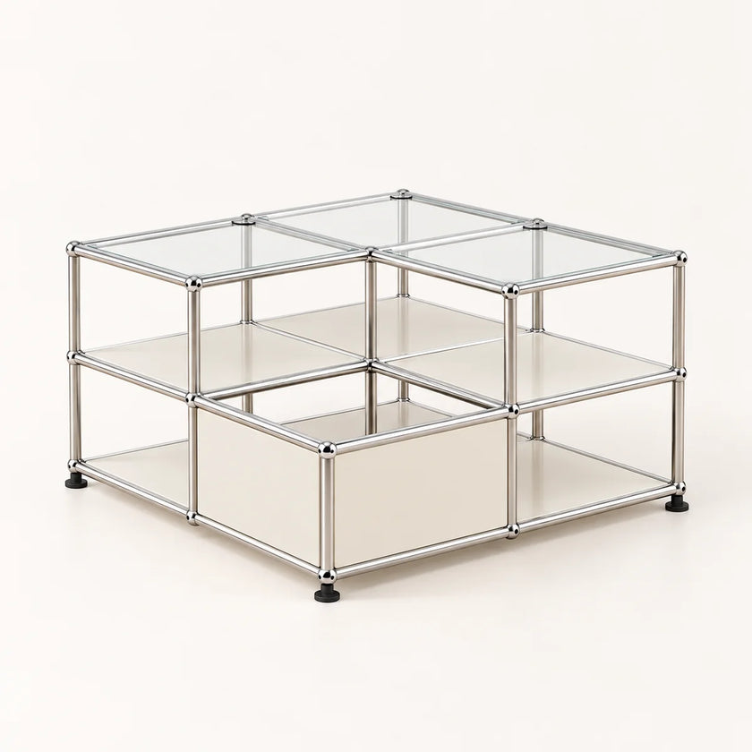 A modular metal and glass storage organizer with square compartments, featuring a stainless chrome frame, clear glass panels, and black rubber feet on a light beige background.