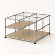 A modular two-tier storage organizer with a chrome metal frame, clear glass panels on the top, and beige shelves on the bottom, shown on a light cream background.