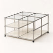 A modular storage organizer made of a chrome-finished metal frame with clear glass panels and cream-colored shelves, shown on a light beige background.