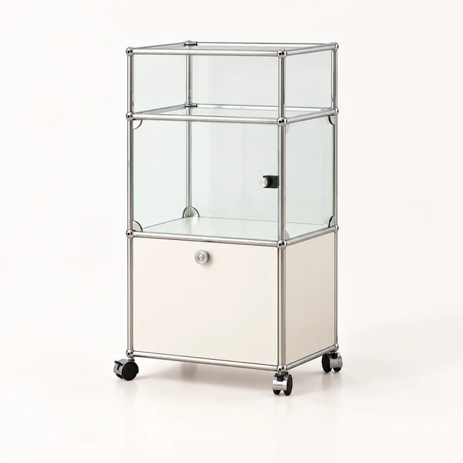 A three-tier glass display case on a wheeled base with a cream-colored lower cabinet door and a chrome metal frame, shown on a clean white background.