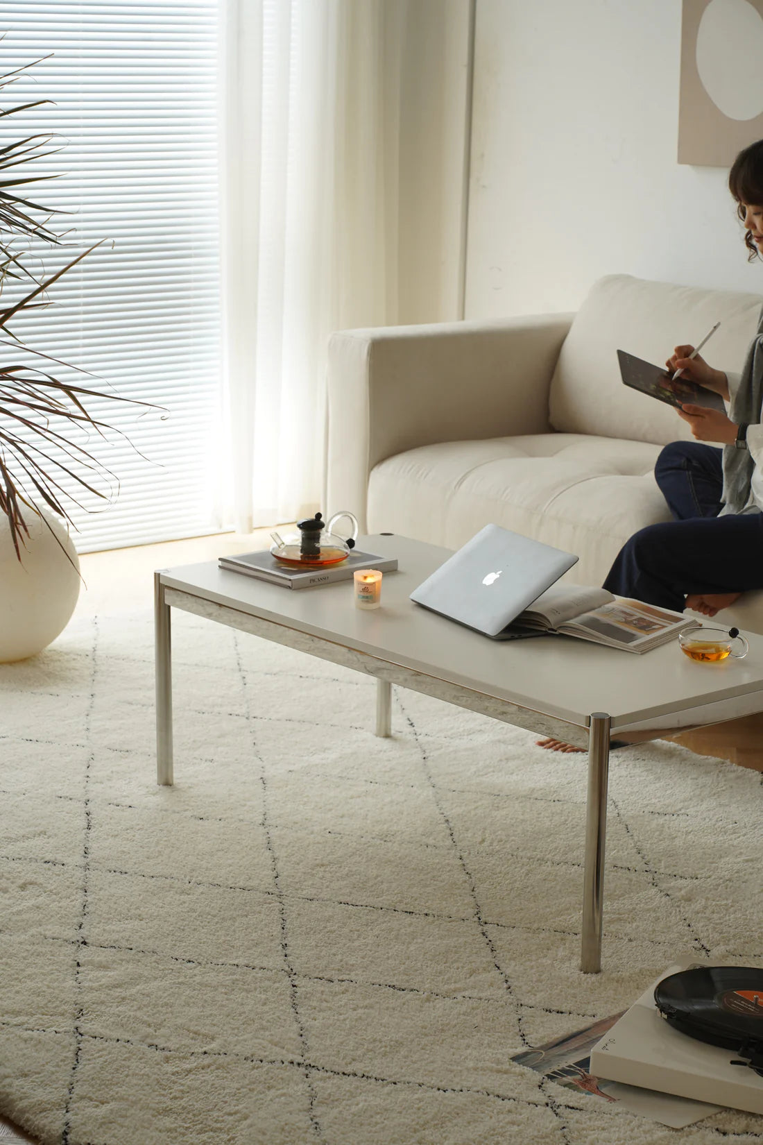 Women sitting on a beige sofa reading a book in a modern living room with a replica USM coffee table.
