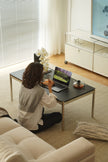 Women sitting on a couch in a living room using a laptop with coffee table.