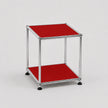 A modern two-tier modular side table with a chrome metal frame and ruby red panel shelves, set against a neutral light gray background.