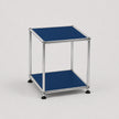 A modern two-tier modular side table with a chrome metal frame and steel blue metal-covered shelves, shown on a light gray background.