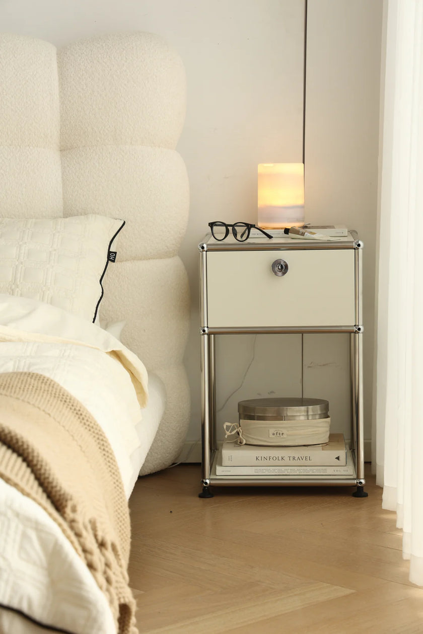 Inspired recreation USM modular nightstand next to a bed with a lamp, books, and glasses on top.