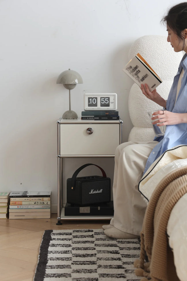 Lady reading a book in a cozy room with a replica USM modular nightstand and lamp.