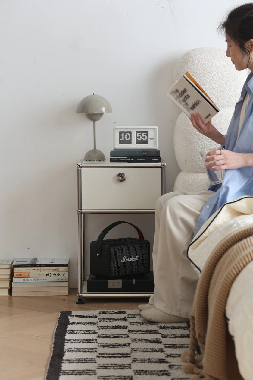 Lady reading a book in a cozy room with a inspired recreation USM modular nightstand and lamp.
