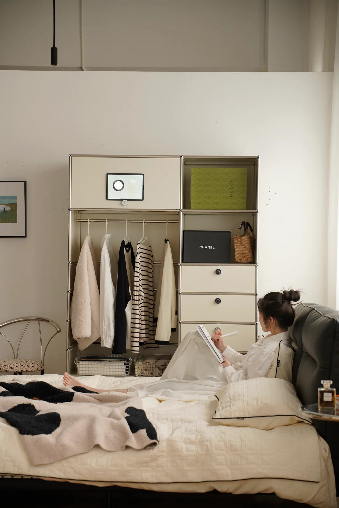 Lady lying on a bed reading a book in a room with a replica USM modular wardrobe and desk.