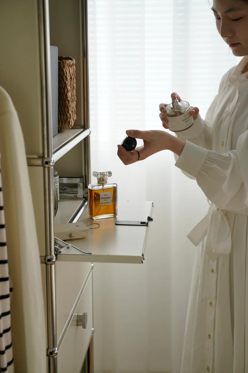Lady in a white robe holding a small container next to a refrigerator with a bottle of perfume on a inspired recreation USM modular wardrobe.