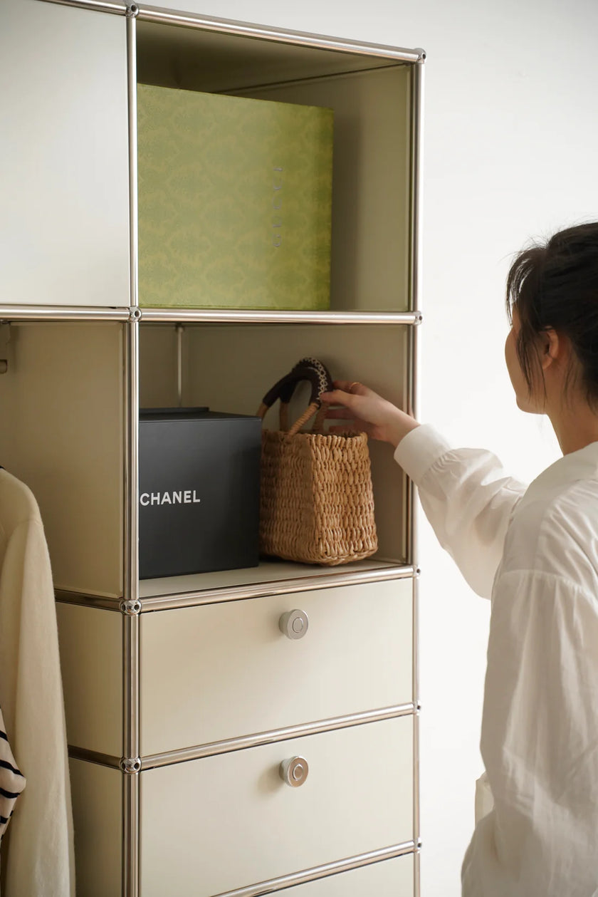 Lady reaching into a inspired recreation USM modular cabinet with a Chanel bag and a wicker basket.