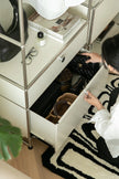 Lady reaching into a replica USM wardrobe cabinet next to a shelf with books and a plant.