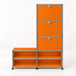 A modular storage cabinet with a orange finish and a chrome metal frame, featuring three drawers on the upper right with round silver knobs and four open shelves on the lower.