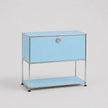 A light blue modular storage cabinet with a chrome metal frame, featuring a single drawer with a round silver knob and an open lower shelf, set against a neutral light gray background.