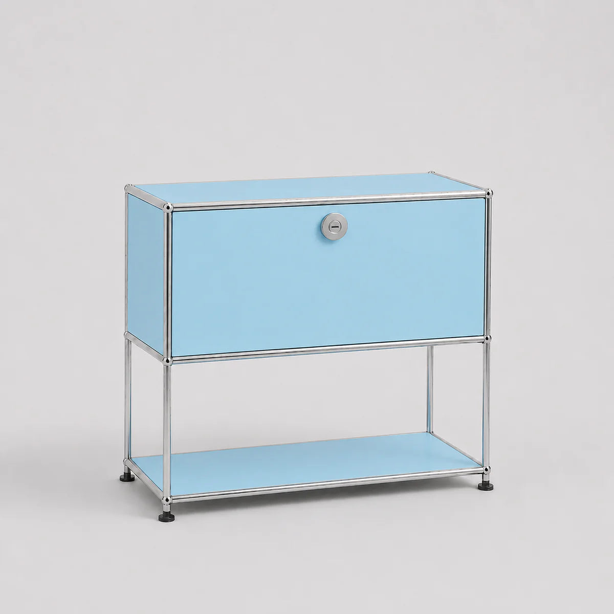 A light blue modular storage cabinet with a chrome metal frame, featuring a single drawer with a round silver knob and an open lower shelf, set against a neutral light gray background.