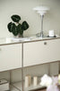 White replica USM modular cabinet with a plant, lamp, and candles on top against a light wall.