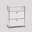 A modern modular two-drawer storage cabinet with a chrome metal frame, white drawer fronts, and a clear glass top shelf, set against a neutral light gray background.