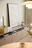 Modern living room with a replica USM modular television, record player, and abstract art on a light-colored wall.