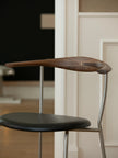 A modern wooden dining chair with a curved dark brown wood backrest, a black upholstered seat, and a slim silver metal frame, shown in a home interior setting.