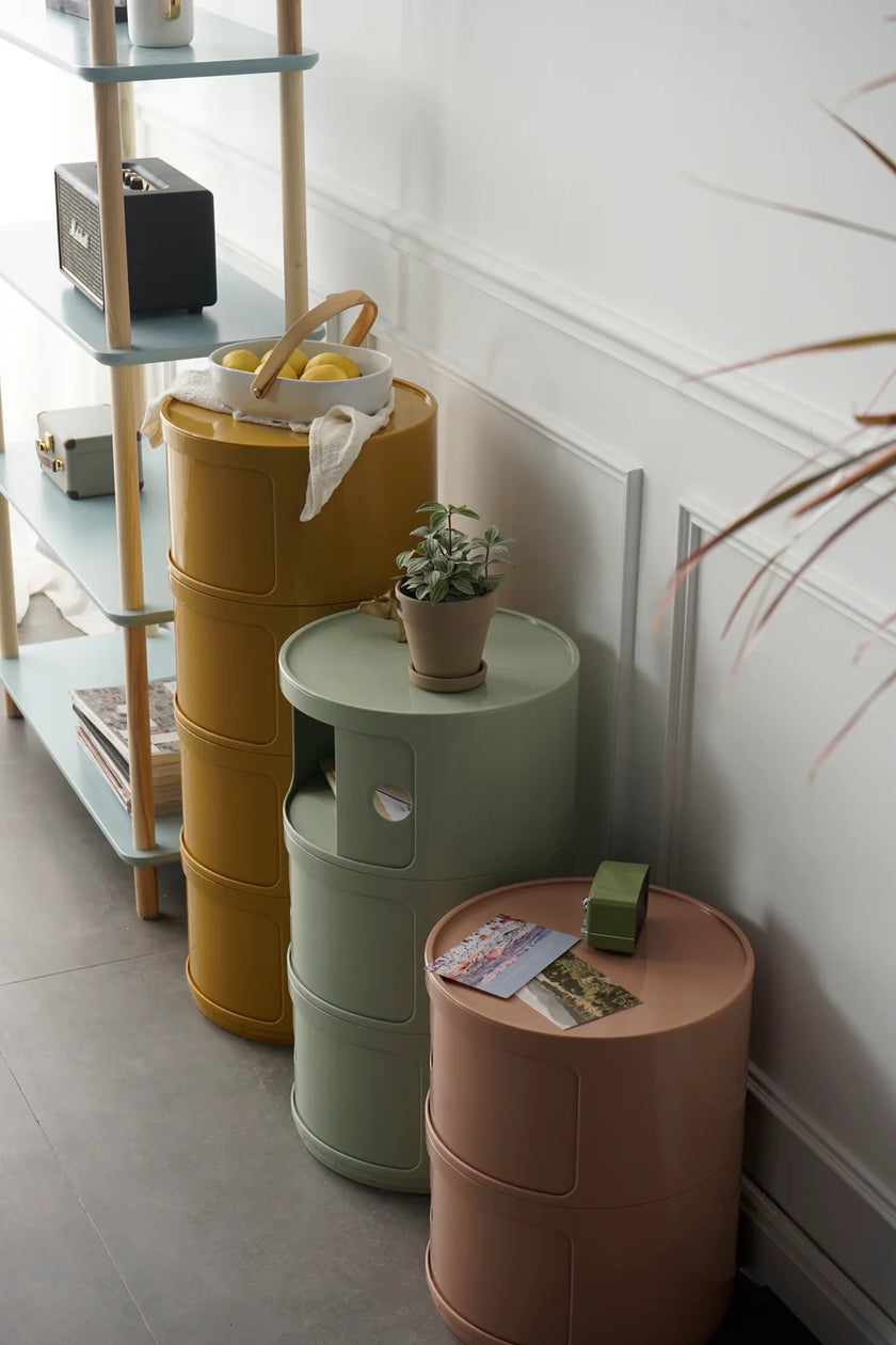 Three cylindrical plastic storage units in yellow, green, and pink against a white wall.