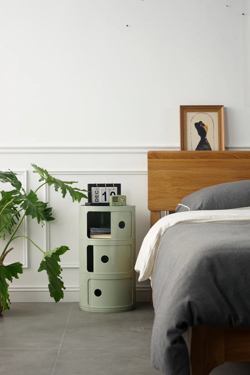Green cylindrical plastic storage containers next to a bed with gray bedding and a wooden headboard.