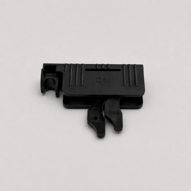 A small black plastic component with molded ridges and a tab-like protrusion, photographed on a plain light gray background.