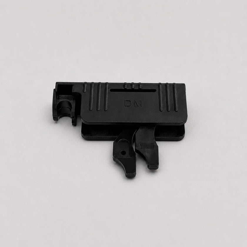 A small black plastic component with molded ridges and a tab-like protrusion, photographed on a plain light gray background.
