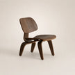 A mid-century modern wooden chair with a curved plywood seat and backrest, shown from a three-quarter angle on a light beige background.