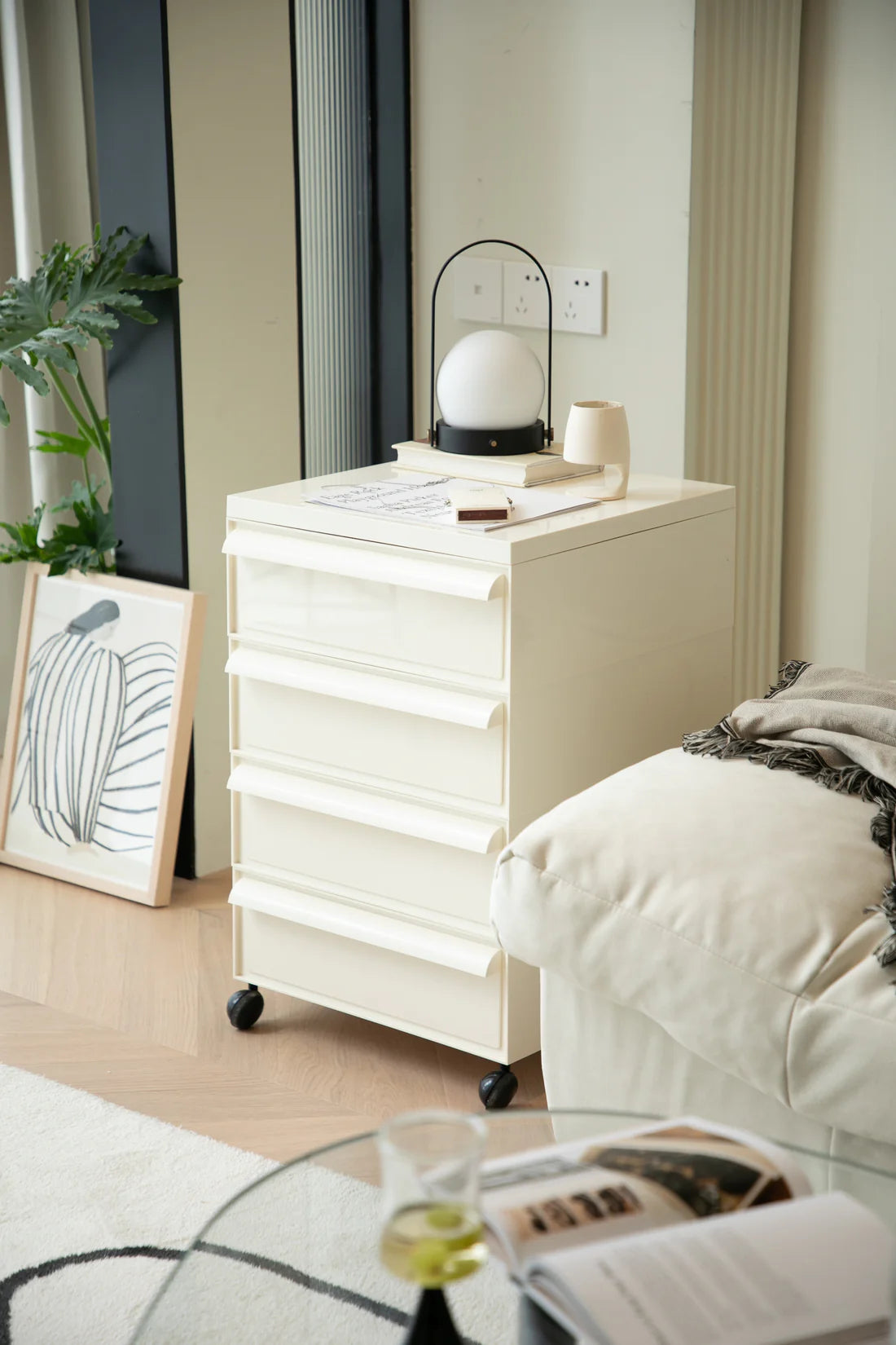 White nightstand with a lamp and books next to a bed in a bedroom setting.