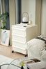White nightstand with a lamp and books next to a bed in a bedroom setting.