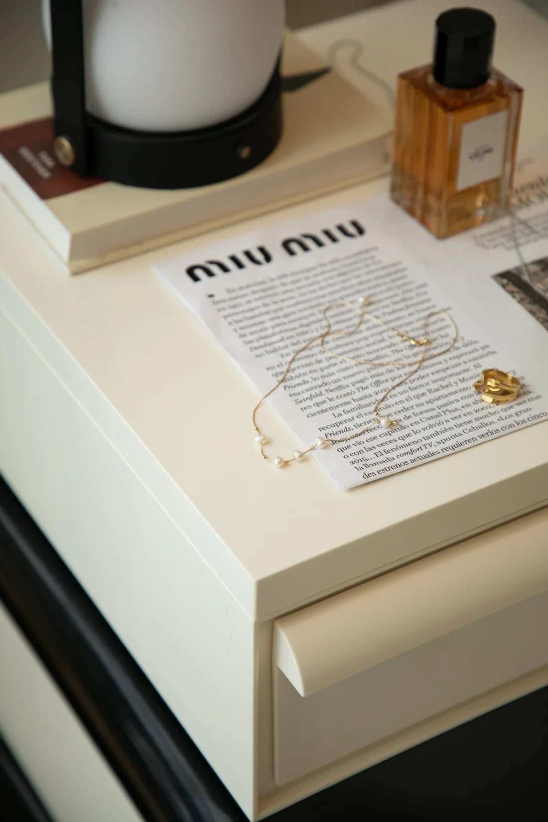Storage containers Miu Miu paper on a white surface with a bottle of perfume and a lamp in the background.