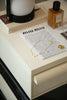 Storage containers Miu Miu paper on a white surface with a bottle of perfume and a lamp in the background.