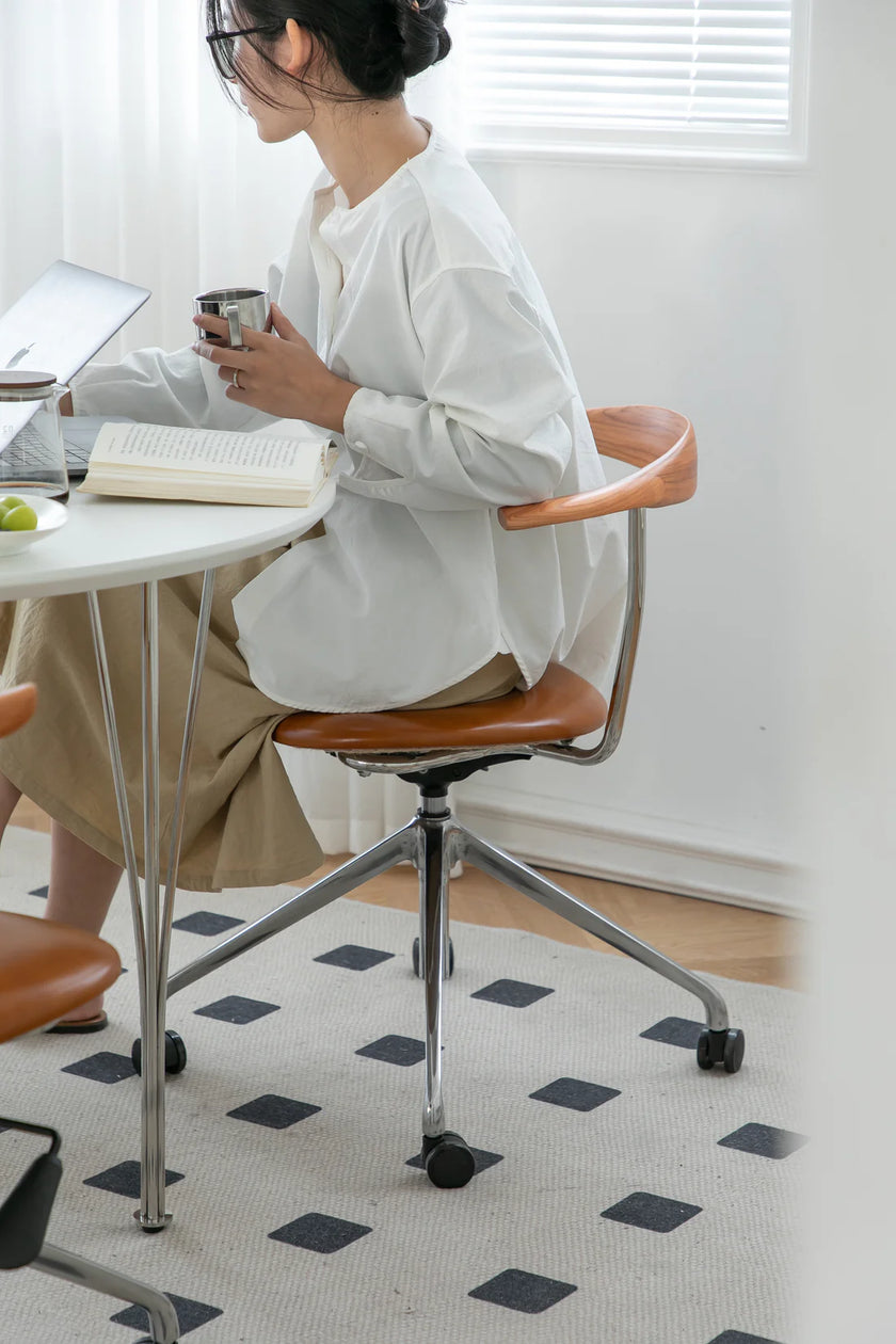 Lady sitting at a desk desk with a book and cup, wearing a white shirt and brown skirt.
