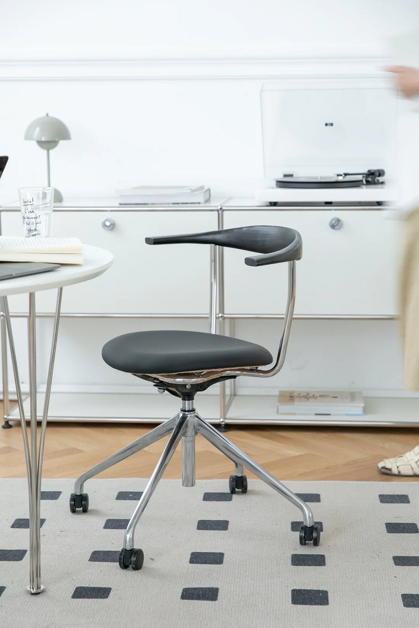 Modern office desk chair with a small table attached to the backrest in a minimalistic office setting.