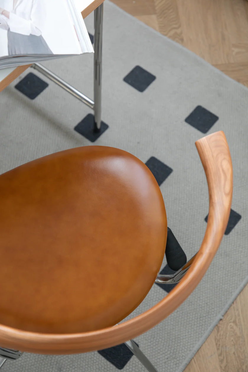 Brown dining chair with wooden armrest on a gray rug with black diamond patterns