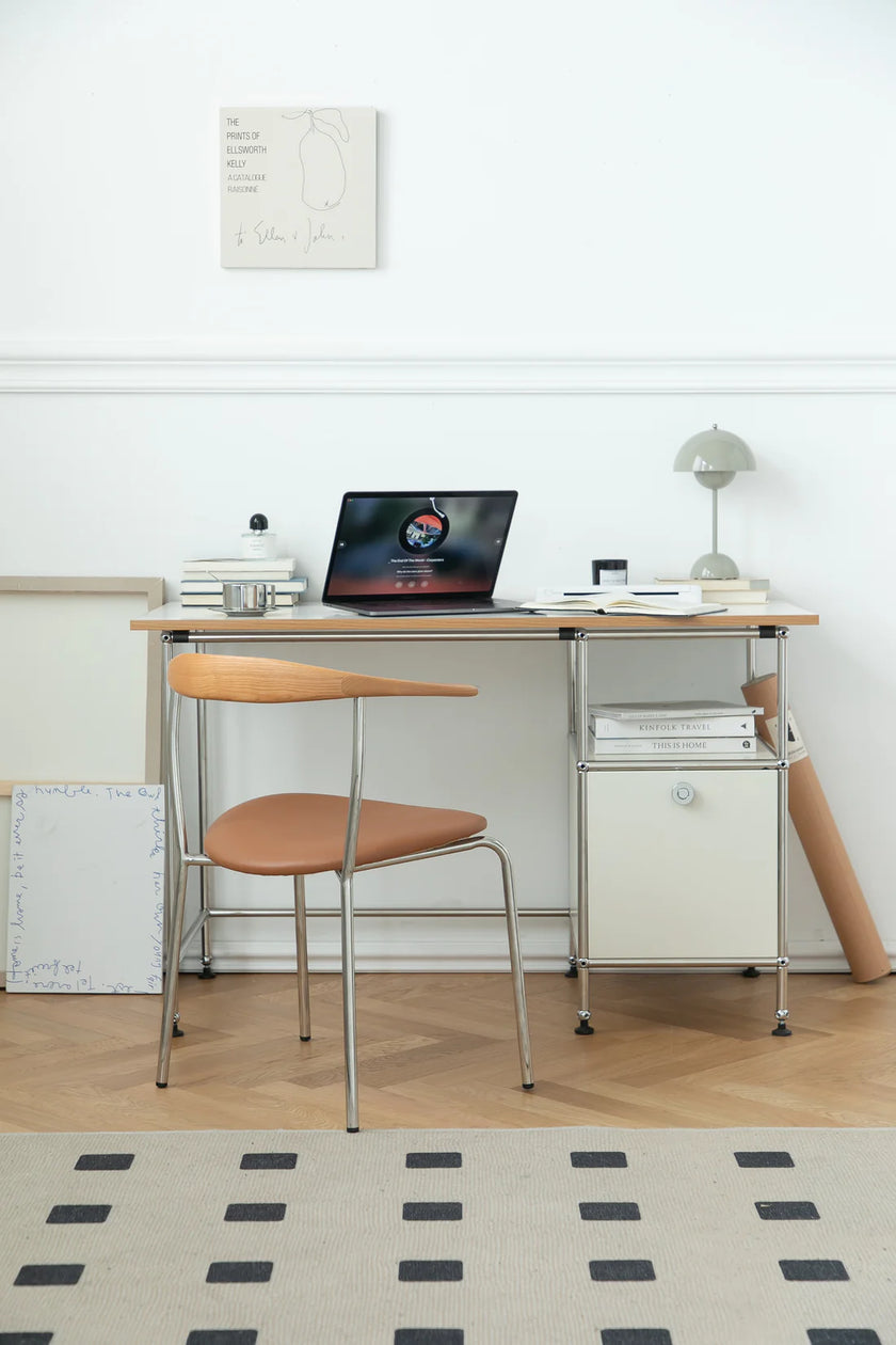 Small desk with a desk computer chair, laptop, and other items in a room with a white wall and wooden floor.