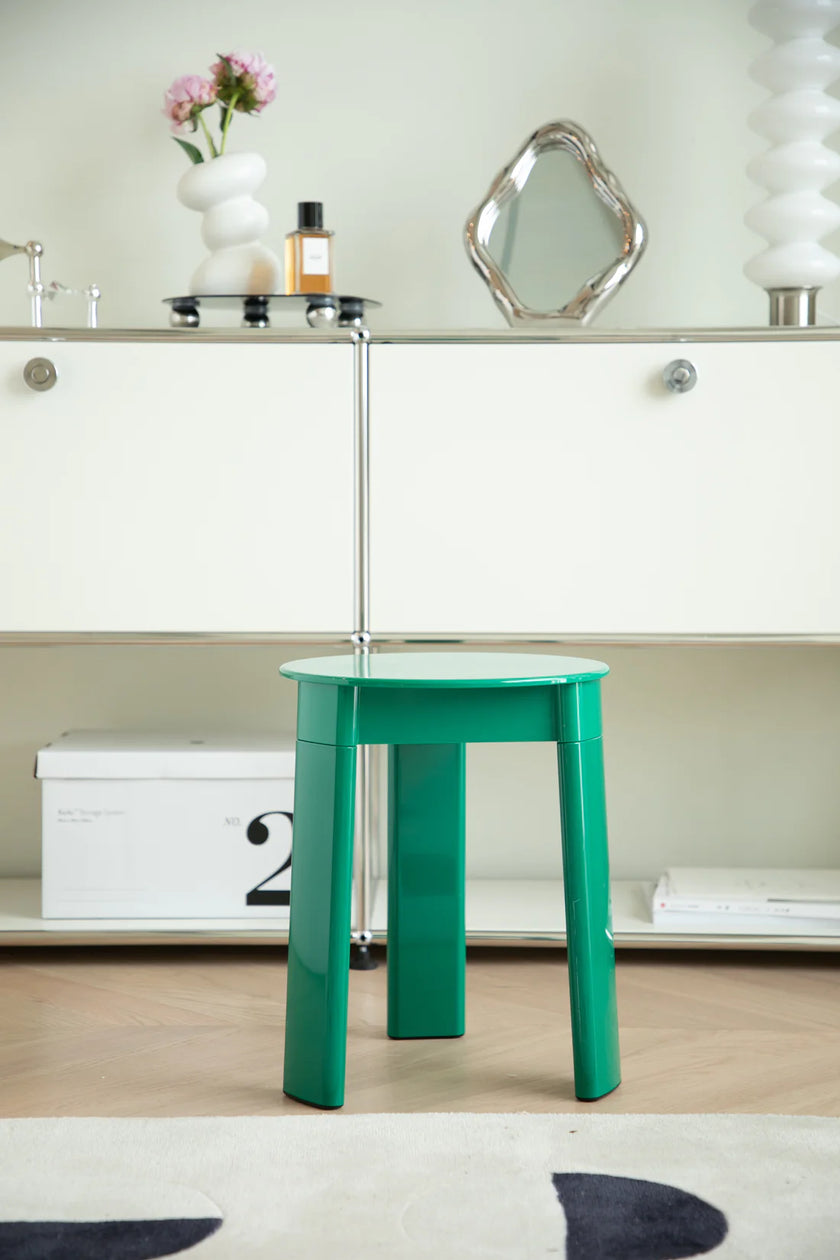 Green plastic bathroom stool in a room with a mirror and decorative items on a shelf.