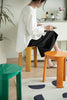 Lady sitting on a small orange bathroom stool in a room with a green shower stools and a plant.